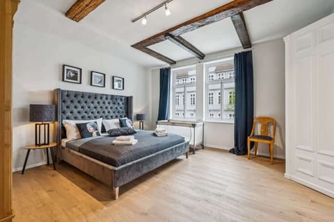 Du schläfst in einem großzügigen Zimmer mit elegantem Design, hohen Fenstern und einem komfortablen Kingsize-Bett mit gepolstertem Kopfteil. Falls du mit Kind anreist, stellen wir gerne kostenlos eine Reisebettchen und einen Hochstuhl dazu.