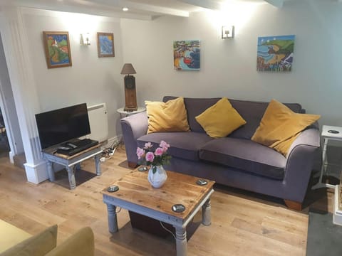 Sitting room with wooden floors. TV, coffee table grey sofa with yellow cushions