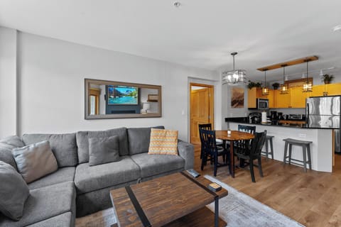 The living area features a mounted smartTV over a gas fireplace, a queen sleeper sofa, and access to the balcony.
