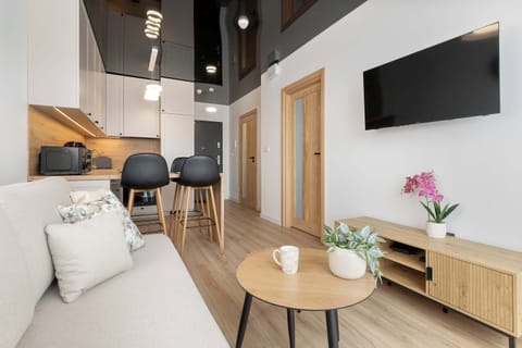 A bright living room with a small round table, chairs, and a TV mounted on the wall.