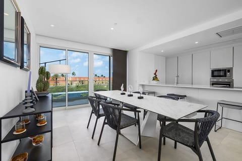 Your sleek dining space invites you to gather around the marble-topped table, while natural light pours through floor-to-ceiling windows, revealing colorful neighborhood views and the sparkling pool beyond.