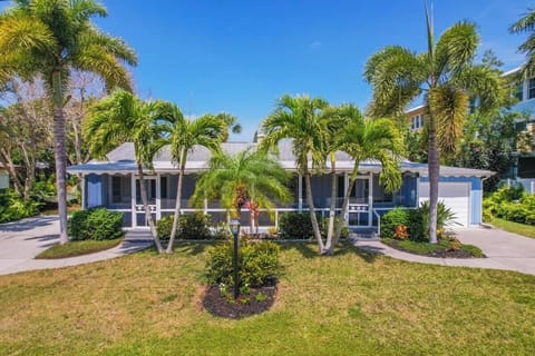 Single-story home with a screened front porch, surrounded by palm trees, and a curved walkway leading to the entry.