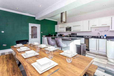 Inviting dining area with a rustic wooden table and modern green kitchen, perfect for gatherings!