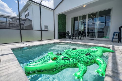 Splash around in your private screened-in pool featuring a playful crocodile float, modern pavers, and a cozy outdoor seating area!