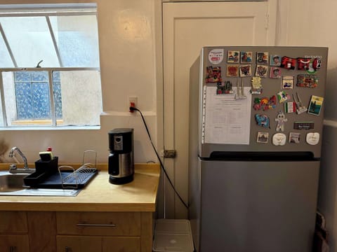 Cocina (tarja para lavar trastes, cafetera, mueble de madera, bote de basura blanco, escurridor de trastes negro y refrigerador)