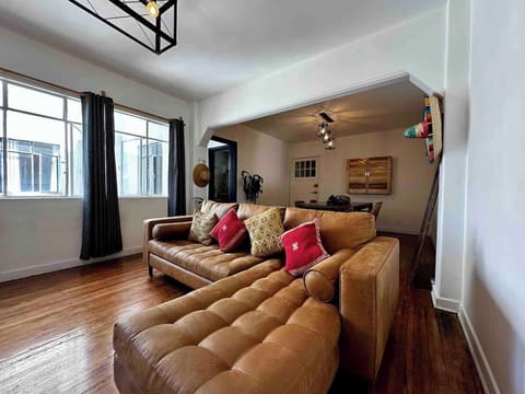 Sala de estar vista desde la esquina (sofá, cortinero, focos, mesa con 4 sillas, cantina, sombreros de decoración, plantas)