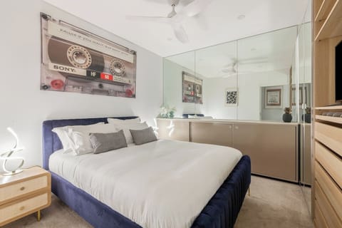 Rest easy in the queen-size bed with soft linens and plush pillows, framed by mirrored storage and artistic touches that add personality and warmth to the bedroom.