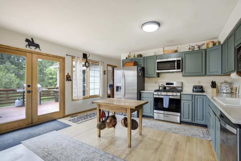 Charming open kitchen and dining space with sage green cabinetry, wood accents, and large windows that fill the room with natural light and forested views.

