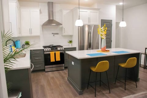 Whip up your favorite meals in our bright, contemporary kitchen featuring sleek appliances, ample counter space, and charming yellow bar stools for a lively touch.