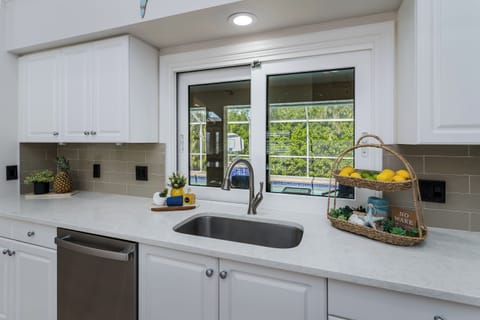 Step into this bright, modern kitchen where you'll love preparing meals with fresh produce from the charming tiered basket. Natural light pours through French doors leading to your outdoor space, while sleek white cabinetry and contemporary fixtures make c