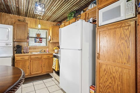 A compact, rustic kitchen featuring wood-paneled walls, a corrugated metal ceiling, wooden cabinetry, and essential appliances including a white refrigerator and an over-the-range microwave