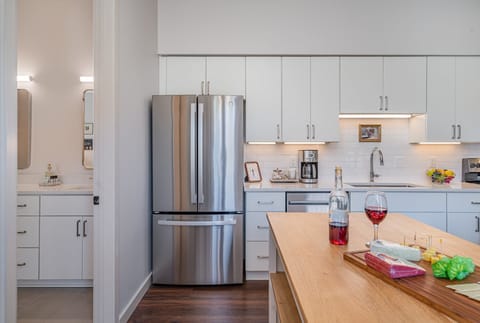 Unit 1: Kitchen with sleek white cabinetry, stainless steel appliances, and a butcher block island, perfect for preparing meals or enjoying a quick bite.