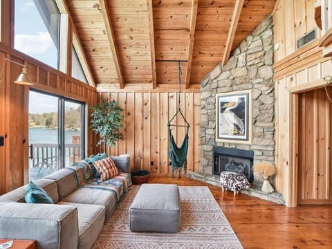 Step into the bright and airy living room of this stunning A-frame lakehouse chalet, where modern comfort meets cozy charm. A low, plush modern sofa invites you to relax beneath soaring vaulted ceilings, while a stylish green hanging chair adds a playful,