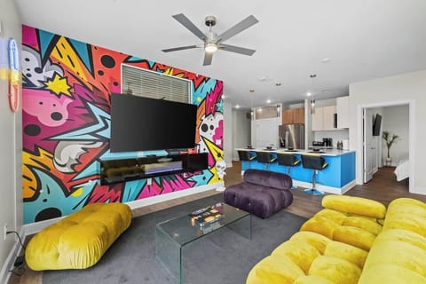 - Colorful living room with bold mural and comfy seating 
- Large TV and vibrant design for entertainment nights 
- Open-concept layout perfect for fun group getaways 