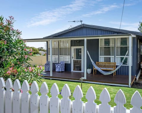 A white picket fence frames the front garden and shaded veranda—an inviting welcome to this classic beach shack..