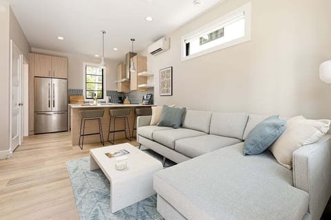 The living room features a large smart TV mounted above a stylish media console, a soft sectional sofa, and a chic coffee table. With warm wood floors and plenty of natural light, it's a perfect spot to relax and recharge.