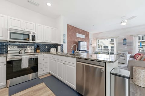 Modern coastal kitchen with sleek stainless-steel appliances, granite counters, and blue tile backsplash. Bright and open to the living area, it’s perfect for cooking, entertaining, and enjoying beachside comfort with effortless style.