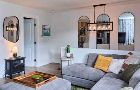 Cozy up in the living room with a plush sectional, colorful pillows, and stylish mirrors. A faux wood stove with warm ambient light adds charm, while modern décor and open flow make this the perfect place to relax after a day out.