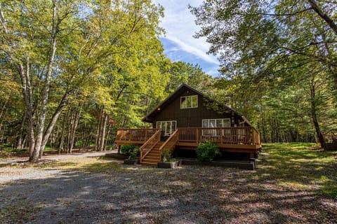 Charming Poconos cabin exterior with a large wooden deck, nestled in the trees for a private mountain escape.