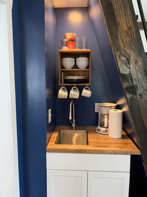 Kitchen has a coffee maker, dishes, cups and mugs