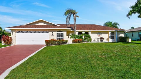 Front view of Villa Just Chill in Cape Coral with double garage, red driveway and well-kept front yard with tropical landscaping