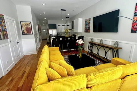 Large bright sunny living room with high ceilings and built-in lighting, 65 inch TV with Roku, oversize plush marigold yellow corduroy sectional couch, and stunning artwork.