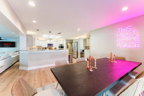 This stylish, modern dining space offers the perfect spot to enjoy meals or relax, highlighted by vibrant neon lighting and a seamless flow into the open kitchen. The cozy atmosphere makes it an ideal retreat for any occasion.
