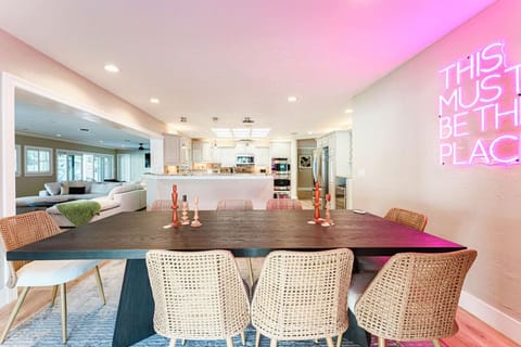 Brighten up your meals with this stylish dining area, featuring modern wicker chairs, a striking neon sign, and a seamless flow into the kitchen and living spaces. Perfect for both intimate gatherings and lively dinners.