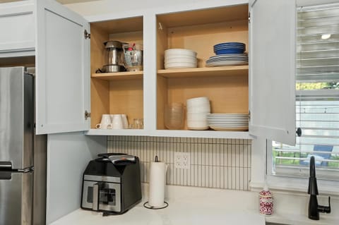 Fully stocked kitchen cabinets with dishes, bowls, mugs, glasses, colander, blender, and coffee machine—everything you need to cook and dine comfortably just like home.