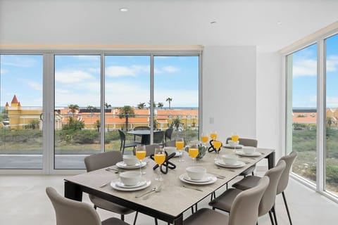 Start your mornings at this elegant dining table with fresh juice and coffee, as floor-to-ceiling windows frame panoramic views of palm trees, rooftops, and the sparkling sea beyond.