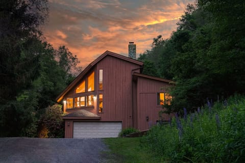 As golden hour hits, Cosmic Ridge Retreat glows from within—your cozy mountain hideaway framed by wild lupines and woodland charm.