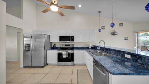 Modern, fully equipped kitchen with white cabinetry, blue countertops, stainless steel appliances, and ceiling fan – perfect for self-catering on vacation.