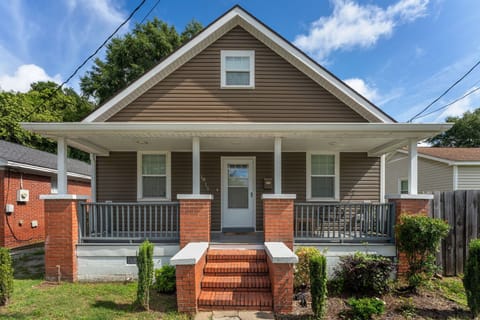 Brown siding, one-and-a-half-story house. Gray porch rail, red brick pillars.