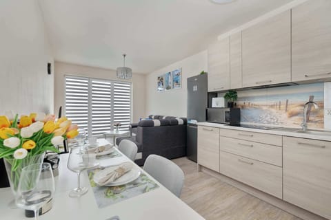 A kitchen and dining area with light wood cabinets, tulips in a vase, and a neatly set table for four people.