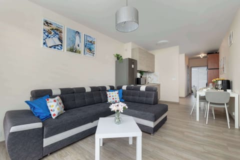 A living room with a dark gray sectional sofa, a small white coffee table, and decorative wall art above the couch.
