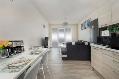 A modern open-plan kitchen and dining area with white and wood tones, stylish chairs, and ample lighting.