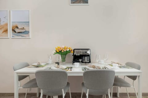A dining space with a long white table, cushioned gray chairs, and a cheerful bouquet of tulips at the center.