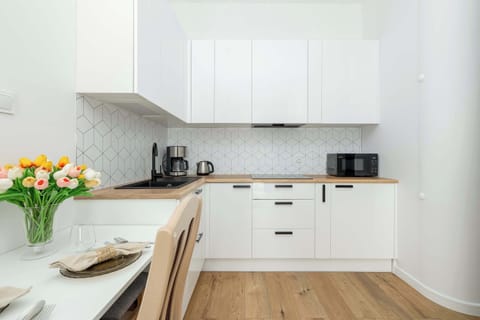 A modern kitchen with white cabinetry, a wooden countertop, and essential appliances including a microwave and coffee machine.