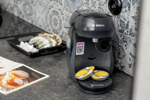 A kitchen countertop with a black coffee maker and fresh ingredients on display. The backsplash has a textured, stone-like pattern.