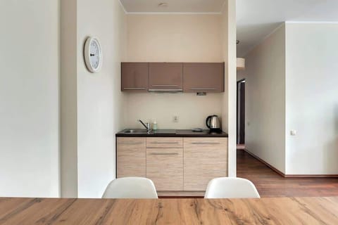 A practical kitchenette featuring a sleek combination of wood and beige cabinetry. The compact design includes a kettle and sink, perfect for preparing quick meals. A wooden dining table with chairs adds functionality and charm.