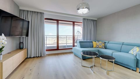 A spacious and open living room with a comfortable blue sectional sofa, a dining table, and large windows providing plenty of natural light.
