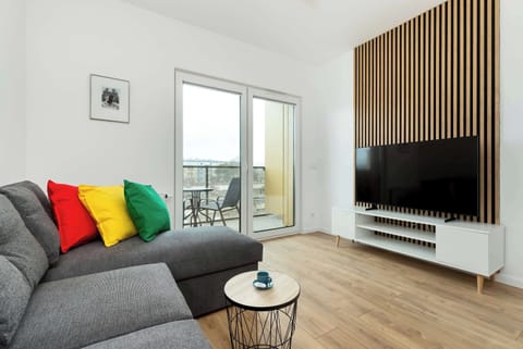 A cozy living room with a grey sofa, wooden accents, and a large TV—perfect for relaxing evenings. Natural light flows in through wide windows.
