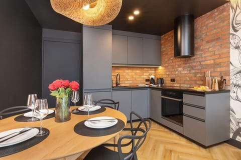 A stylish kitchen and dining area with dark cabinetry, brick walls, and modern lighting.