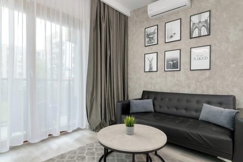 Air-conditioned lounge area with black sofa, coffee table, TV and access to balcony.