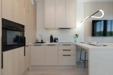 A modern kitchenette with white cabinets, and full appliances like kettle, oven, stove, offers cooking convenience and interior elegance.