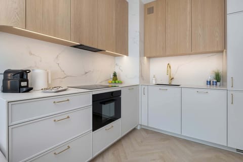 Compact L-shaped kitchen with white cabinetry, wooden accents, and built-in appliances.