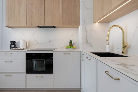 Compact L-shaped kitchen with white cabinetry, wooden accents, and built-in appliances.