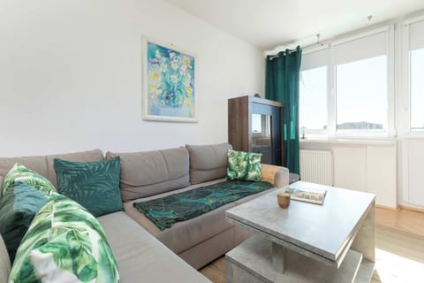 The modern apartment on Piastowska Street in Gdansk offers a spacious living room with a large corner sofa in shades of gray, decorated with pillows with a plant motif, a stylish coffee table and large windows providing plenty of natural light and a 