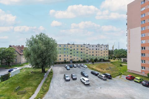 A residential view of a parking lot surrounded by green trees and mid-rise apartment blocks.

