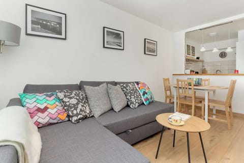 A different angle of the gray sofa in the living room with pillows and a cup placed on the coffee table, with part of a curtain visible.

